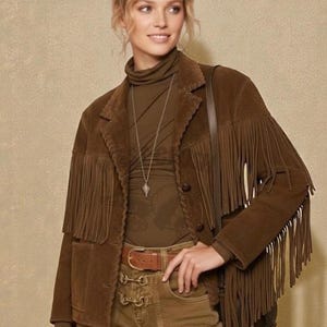 May include: A woman wearing a brown suede jacket with fringe detailing, a brown turtleneck, and matching pants. She is also wearing a brown belt and a silver necklace. The jacket has a classic Western style.