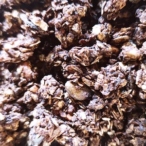 Könnte beinhalten: Nahaufnahme einer Schüssel mit dunkler Schokoladen-Granola. Die Granola besteht aus Haferflocken, Nüssen und Schokoladenstückchen.
