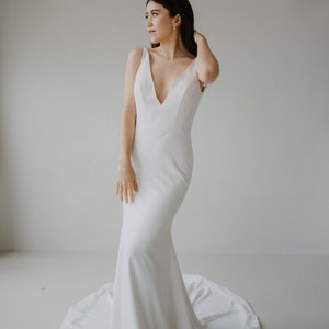 May include: A woman wearing a white, sleeveless, V-neck wedding dress with a fitted bodice and a flowing skirt.