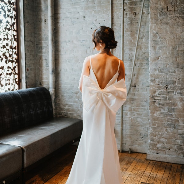 Saravine: minimal column sheath wedding bridal gown with low back, detachable bow train, and thin straps