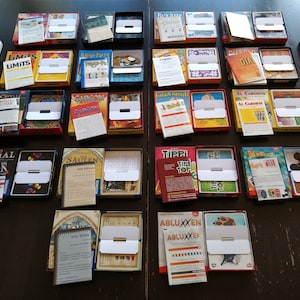 Puede incluir: Una colección de 16 juegos de mesa diferentes en sus cajas originales. Los juegos están dispuestos en cuatro filas de cuatro cajas cada una. Las cajas son todas de diferentes colores y tienen diferentes diseños. Algunos de los juegos incluyen "Limits", "Cargo", "Genial", "Die Tore", "Tippi Top", "Abluxxen", "Saulen", "Fe", "Kribbeln", "Al Caboune", "Dial", "Pingu-Pa-Pa", "Bist Du Ein Narr", y "Ruzan".