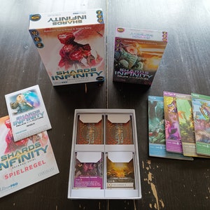 Pode incluir: Um jogo de tabuleiro chamado "Shards of Infinity" com duas caixas, um livro de regras, quatro cartas e quatro mangas para cartas. As caixas são azuis e pretas com um design futurista. O livro de regras é preto e branco com o título do jogo na capa. As cartas são coloridas e apresentam diferentes personagens e designs.