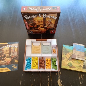 May include: A board game called "Beer & Bread" with a brown box, a game board, and various game pieces. The box has a picture of two people sitting at a table with a beer and bread.