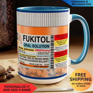 May include: A white ceramic mug with a blue handle and rim, featuring a humorous prescription label design. The label reads "Fukitol Oral Solution" with a list of side effects. The mug is dishwasher and microwave safe.