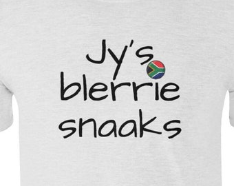 Può includere: Maglietta bianca con testo nero che recita "Jy's blerrie snaaks" con una piccola grafica della bandiera sudafricana.