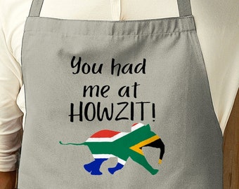 May include: A grey apron with the text "You had me at HOWZIT!" and a cartoon elephant with the South African flag on its back.
