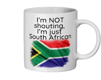 May include: White ceramic mug featuring a black and green South African flag design. The text "I'm NOT shouting, I'm just South African" is printed on the mug.