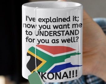 Könnte beinhalten: Eine weiße Keramiktasse mit einem schwarz-weißen Textdesign, das "Ich habe es erklärt; jetzt willst du, dass ich es auch für dich verstehe?" lautet. Die Tasse zeigt außerdem eine Grafik der südafrikanischen Flagge und das Wort "KONA!!!" in schwarzem Text.