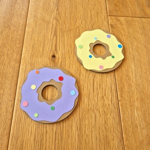 May include: Two paper donuts with colourful sprinkles. One donut is purple with a brown centre and the other is yellow with a brown centre.