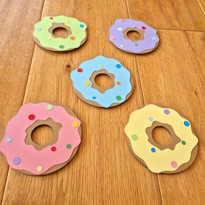 May include: Five paper donuts with different coloured frosting and sprinkles. The donuts are light green, purple, light blue, pink, and yellow.