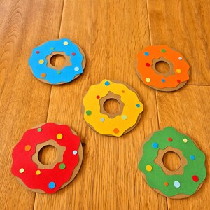 May include: Five paper donuts in different colours: blue, yellow, red, green, and orange. Each donut has a brown centre and colourful sprinkles.