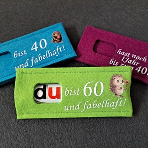 Könnte beinhalten: Drei Filzbanner mit verschiedenen Botschaften und Bildern. Der erste Banner ist blau und sagt "bist 40 und fabelhaft!" mit einem kleinen Bild eines Hundes. Der zweite Banner ist lila und sagt "hast noch 1Jahr bis 40ten!" mit einem kleinen Bild eines Hundes. Der dritte Banner ist grün und sagt "du bist 60 und fabelhaft!" mit einem kleinen Bild eines Igels.