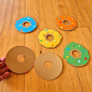 May include: Five paper donuts with colourful sprinkles. Two donuts are brown, one is blue, one is yellow, and one is green.