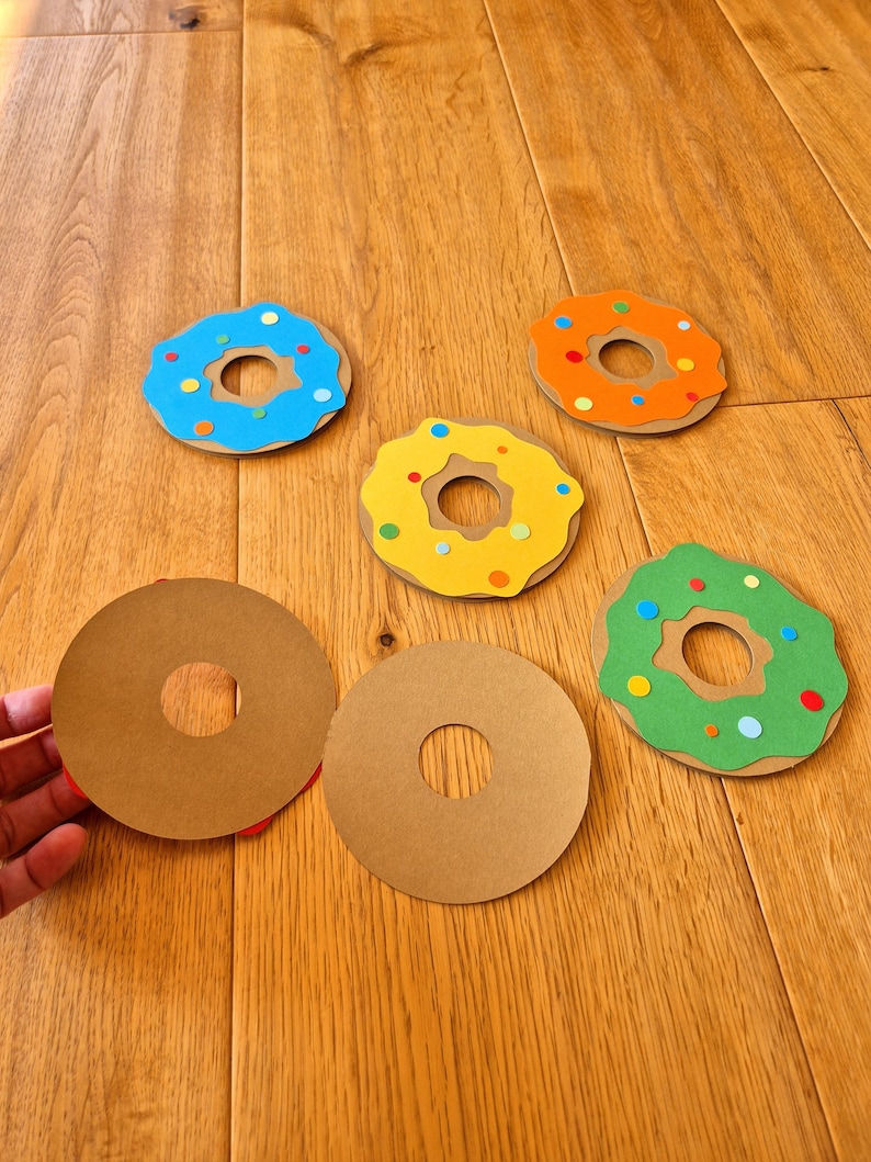 May include: Five paper donuts with colourful sprinkles. Two donuts are brown, one is blue, one is yellow, and one is green.