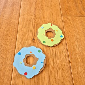 May include: Two paper donuts, one light blue with colourful sprinkles and one light green with colourful sprinkles.