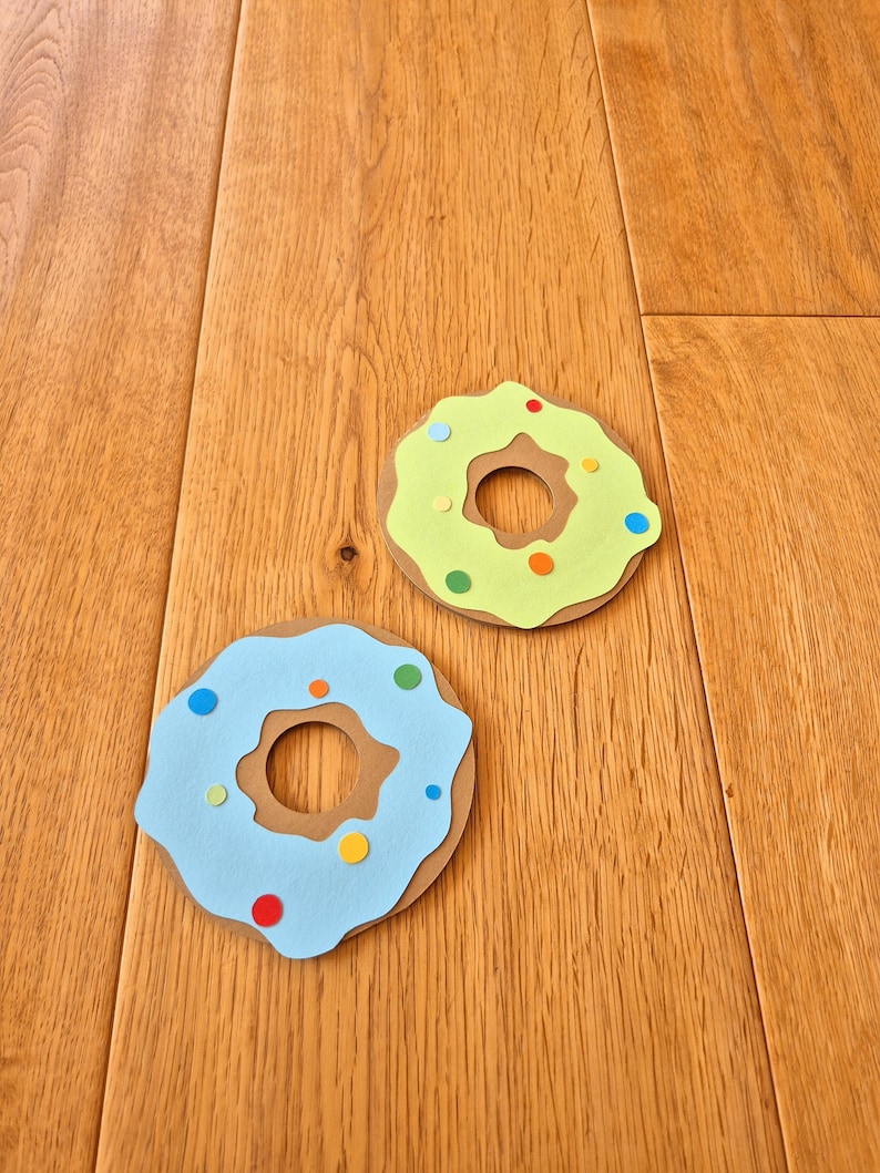 May include: Two paper donuts, one light blue with colourful sprinkles and one light green with colourful sprinkles.