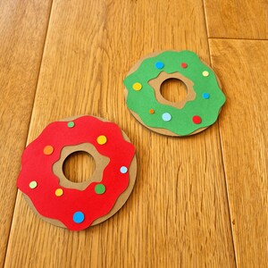 May include: Two paper donuts, one red and one green, with colourful sprinkles. The donuts are on a wooden surface.
