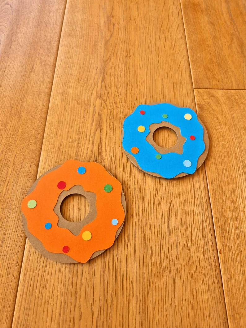 May include: Two paper donuts, one blue with yellow, red, and white sprinkles, and one orange with yellow, red, and blue sprinkles.