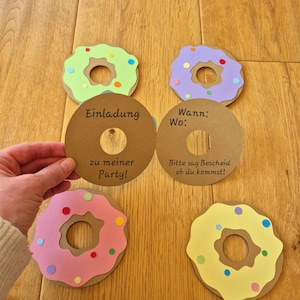 May include: Four brown paper donut-shaped invitations with colourful paper donuts on top. The text on the invitations reads "Einladung zu meiner Party!" and "Wann: Wo: Bitte sag Bescheid ob du kommst!"