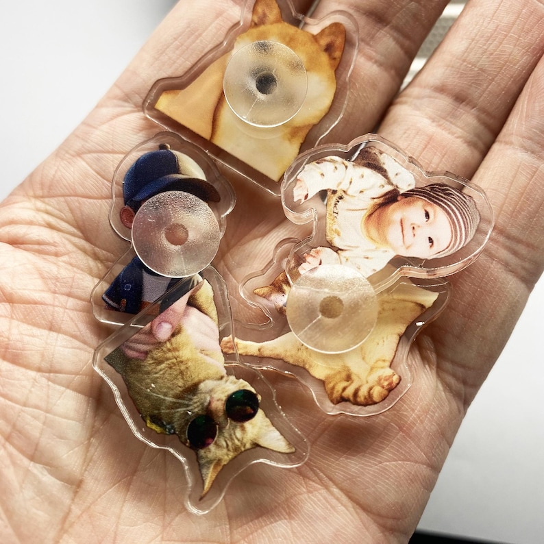 May include: Five clear acrylic charms with different images printed on them. The charms feature a dog, a baby, a cat, and two other images. Each charm has a clear adhesive backing.