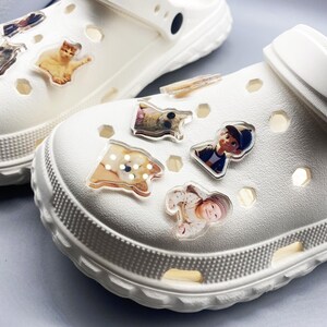 May include: White clogs with various photo charms attached. The charms include a cat, a dog, a baby, and a person.