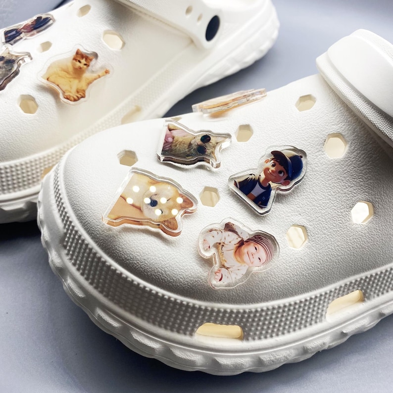 May include: White clogs with various photo charms attached. The charms include a cat, a dog, a baby, and a person.