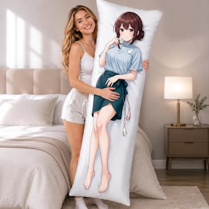 May include: A rectangular body pillow featuring a printed anime-style illustration of a person with brown hair wearing a light blue short-sleeved top and a dark teal skirt. The character has a small white bird emblem on the chest and hanging tassels.