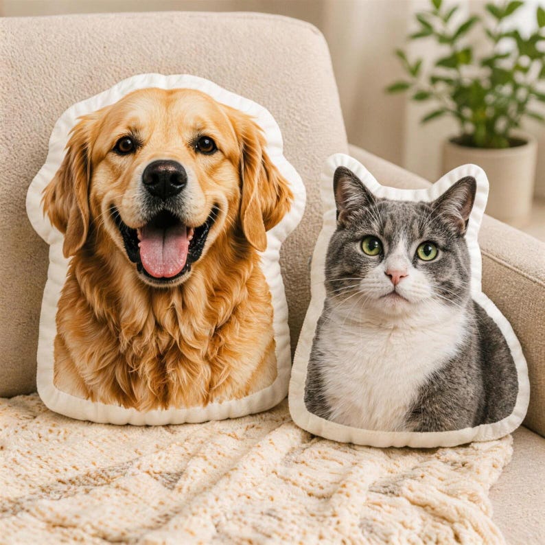 K&ouml;nnte beinhalten: Zwei dekorative Kissen in Form eines Golden Retrievers und einer grau-wei&szlig;en Katze. Das Hundekissen hat ein l&auml;chelndes Gesicht mit herausgestreckter Zunge. Das Katzenkissen hat gr&uuml;ne Augen. Beide Kissen haben einen wei&szlig;en Rand.