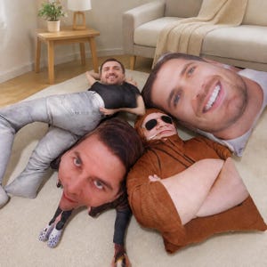 May include: A collection of four custom-shaped throw pillows featuring high-resolution photographic prints of human faces and bodies. The pillows include a person in a black shirt and gray jeans, a person in a brown hoodie, and two large head-only pillows.