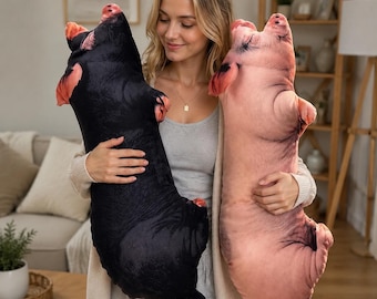 May include: Two plush pig-shaped pillows, one in solid black and one in light pink, featuring realistic printed details including ears, snouts, and tails. These soft, elongated stuffed toys are designed with a lifelike appearance and smooth texture.