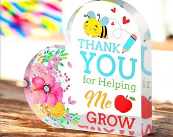 May include: A heart-shaped acrylic paperweight with a floral design and the text "Thank You for Helping Me Grow". A cartoon bee with a pencil is also featured.
