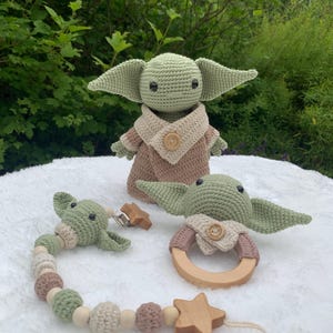 Può includere: Un giocattolo per bambini in crochet verde con un gilet marrone e un anello di legno, un giocattolo per bambini in crochet verde più piccolo con un gilet marrone e una stella di legno con una catena di perline.