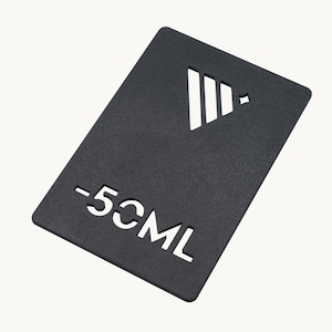 Może przedstawiać: Czarna prostokątna karta z wyciętym wzorem i napisem "-50ML". Wycięty wzór to biały trójkąt z trzema pionowymi liniami i małym rombem. Karta jest na białym tle.