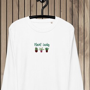 Könnte beinhalten: Weißer Langarm-Pullover mit dem Text "Plant Lady" und einer Reihe von fünf kleinen Topfpflanzen, die auf der Vorderseite gestickt sind.