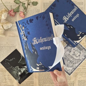 Può includere: Un libro blu scuro con il titolo "Alchemised sentinyu" in lettere argentate, con un disegno di pipistrello e castello. Un nastro bianco è legato attorno al libro. Lo sfondo comprende carta vintage e un busto.
