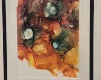 May include: Abstract alcohol ink painting in a black frame. The artwork features a blend of warm colours, including orange, red, and yellow, with accents of green and white. The ink creates a flowing, organic design.