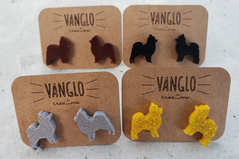 May include: Four pairs of dog-shaped earrings on brown cards with the text "VANGLO creations". The earrings are in brown, black, silver, and yellow glitter.