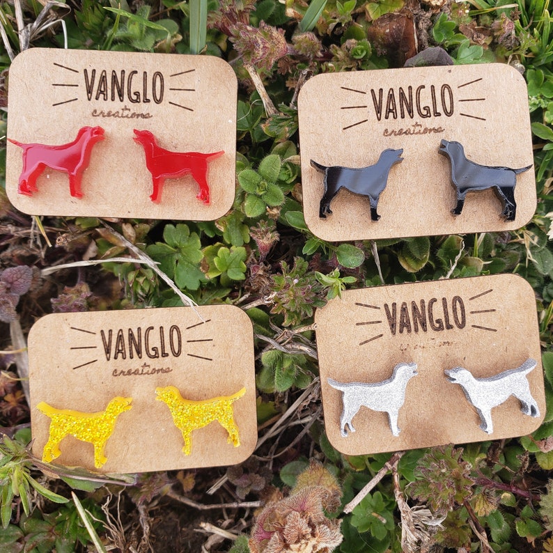 May include: Four pairs of dog silhouette earrings on wooden cards. The cards have the text "VANGLO creations" on them. The earrings are black, red, yellow, and silver.