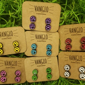 May include: Assortment of eight pairs of paw print stud earrings on brown cards with the text "VANGLO creations". The earrings are in various colors including purple, yellow, blue, red, pink, green, and white.