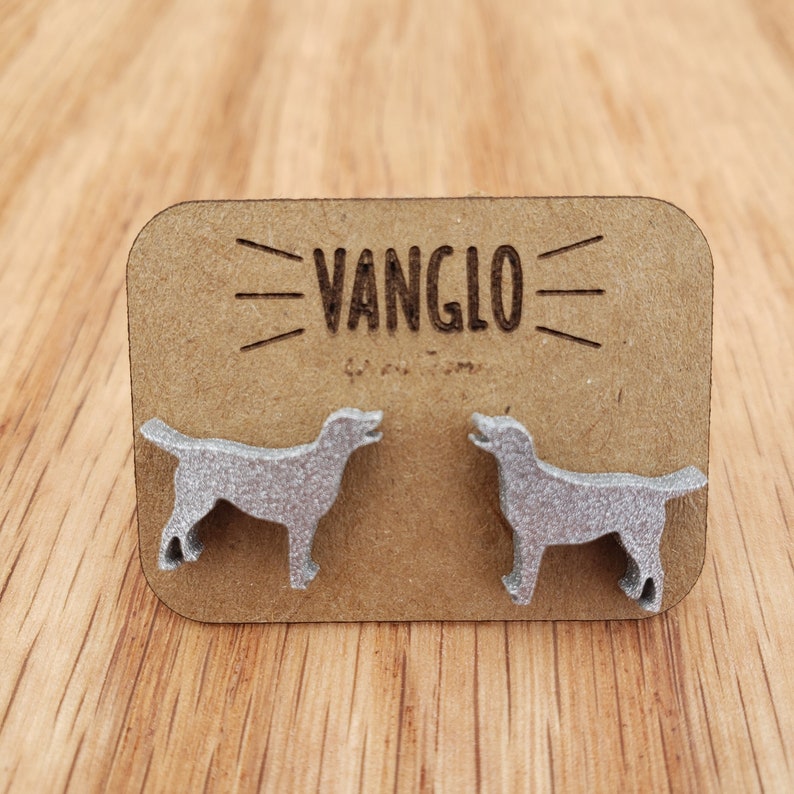 May include: A pair of silver dog-shaped earrings on a brown card with the text "VANGLO" printed on it.
