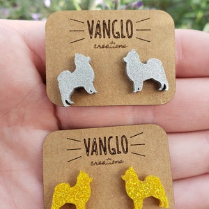 May include: Two pairs of dog-shaped earrings. One pair is silver glitter and the other is yellow glitter. The earrings are on a brown card with the text "VANGLO creations" printed on it.