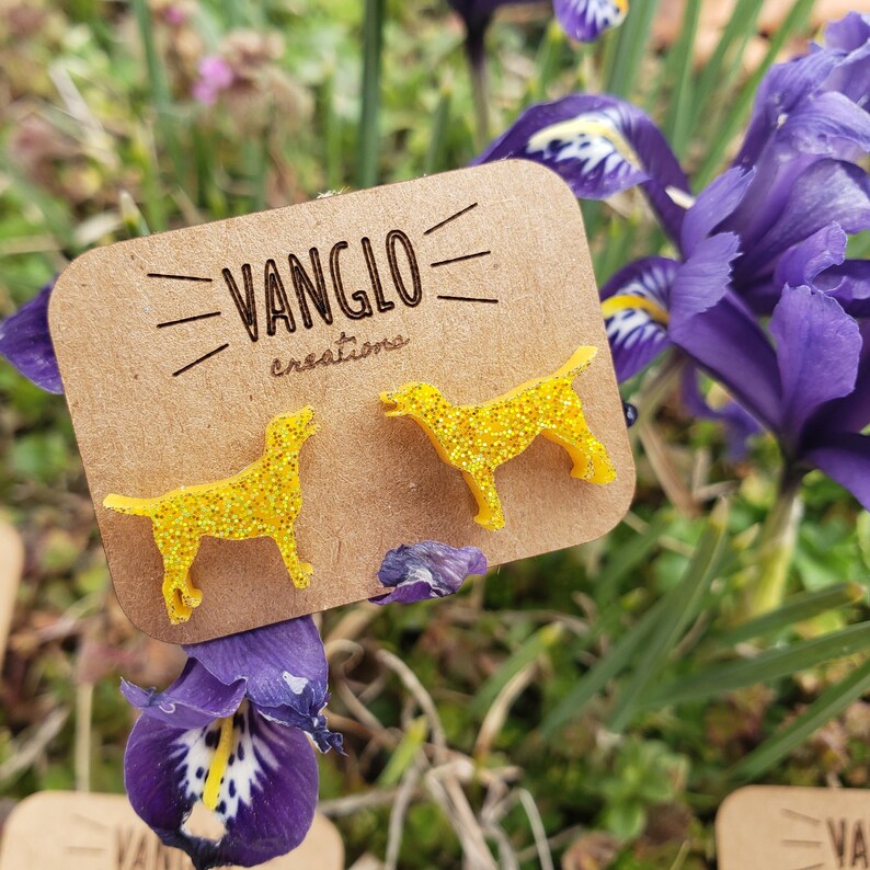 May include: A pair of yellow glitter dog earrings on a brown card with the text "VANGLO creations".