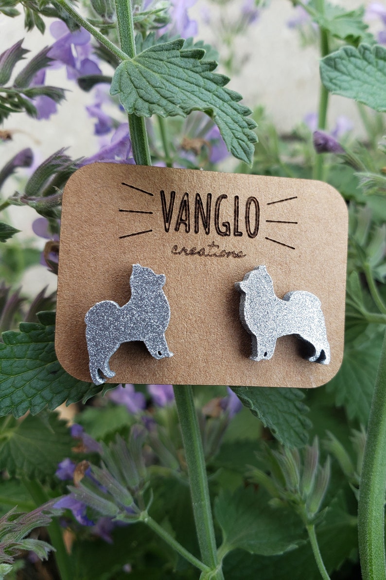 May include: A pair of silver glitter dog silhouette earrings on a brown card with the text "VANGLO creations".
