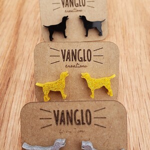May include: Four pairs of dog-shaped earrings on display cards. The earrings are made of acrylic and come in red, black, yellow, and silver. Each card features the text "VANGLO creations".