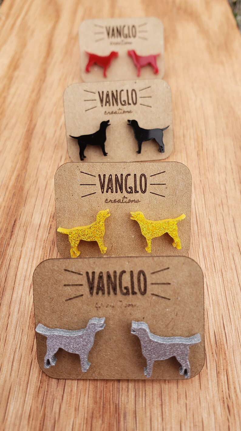May include: Four pairs of dog-shaped earrings on display cards. The earrings are made of acrylic and come in red, black, yellow, and silver. Each card features the text "VANGLO creations".