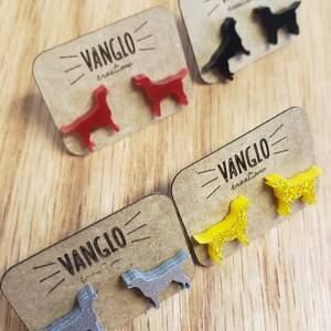 May include: Four pairs of dog-shaped earrings on display cards. The earrings are made of acrylic and come in red, black, yellow, and silver. Each card has the text "VANGLO creations" printed on it.