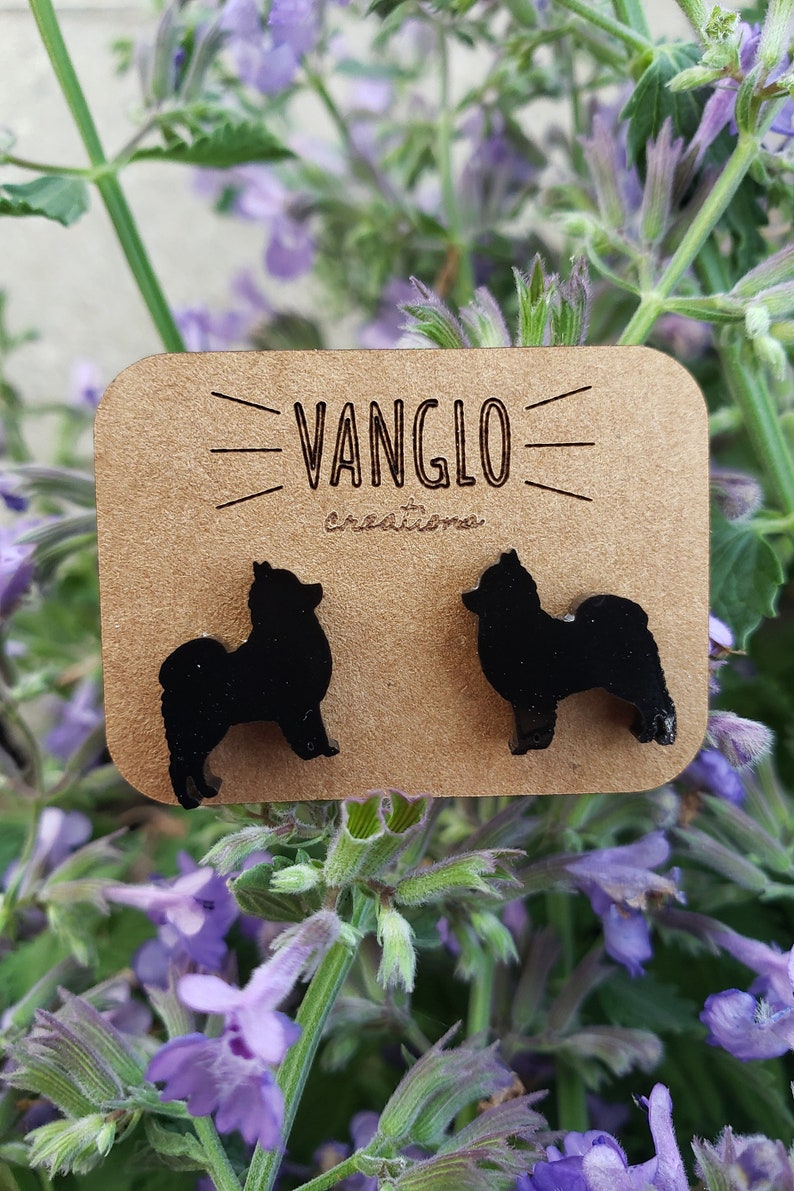 May include: A pair of black wooden earrings shaped like a small dog breed. The earrings are on a brown card with the text "VANGLO creations".