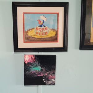 Peut inclure: Trois œuvres d'art encadrées sur un mur bleu clair. La pièce du haut est une peinture abstraite noire, rose et turquoise. La pièce du milieu est un dessin animé encadré de Woody Woodpecker en bébé avec le texte "Born to Peck". La pièce du bas est une peinture abstraite noire, rose et turquoise.