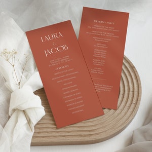 May include: A terracotta-coloured wedding ceremony programme with the names Laura & Jacob printed in white. The programme lists the wedding party, ceremony details, and the order of events.