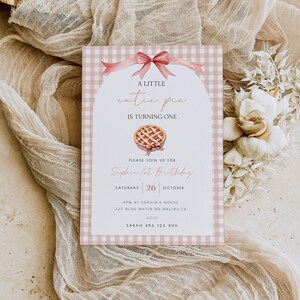 Puede incluir: Una invitación de cumpleaños rosa y blanca a cuadros vichy, con una ilustración de tarta en acuarela. El texto dice "A Little Cutie Pie is Turning One" e incluye los detalles de la fiesta para el primer cumpleaños de Sophia.